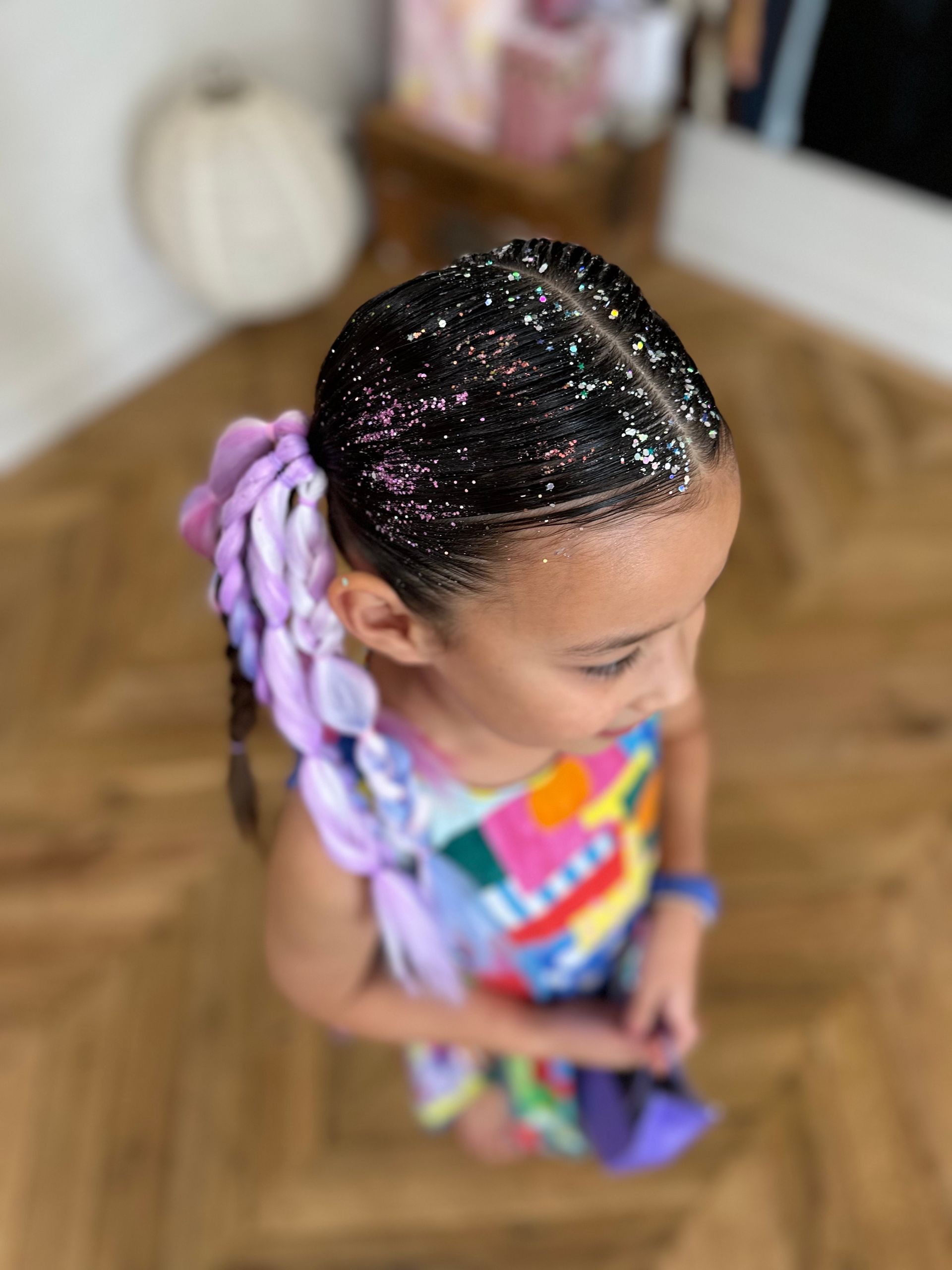 Child with braided hair and colorful dress standing indoors on a wood floor. β Sweet Parties & Braids in Tatton, NSW