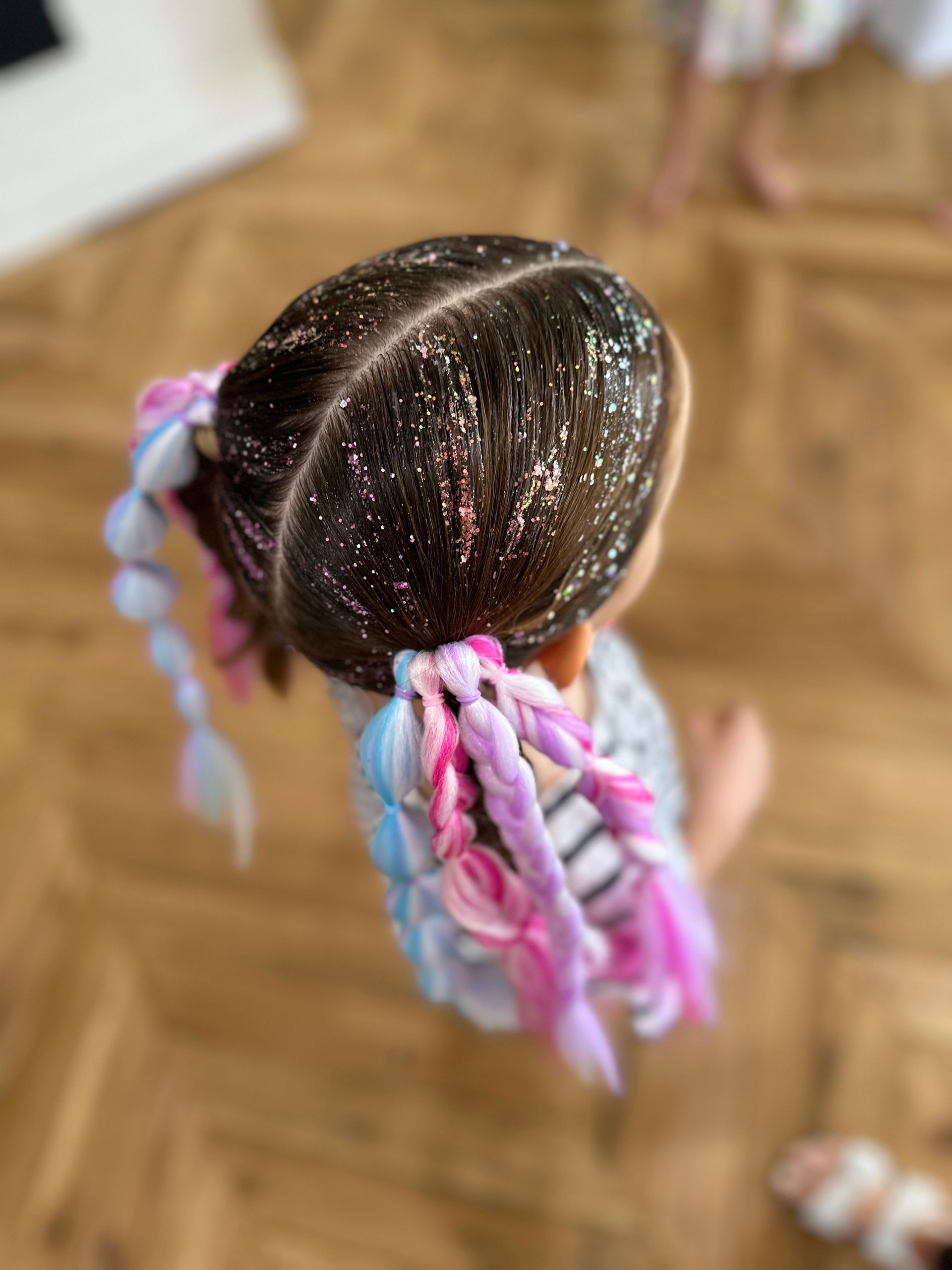 Top-down view of a doll with dark hair in pink and blue braided pigtails on a wooden floor β Sweet Parties & Braids in Tatton, NSW