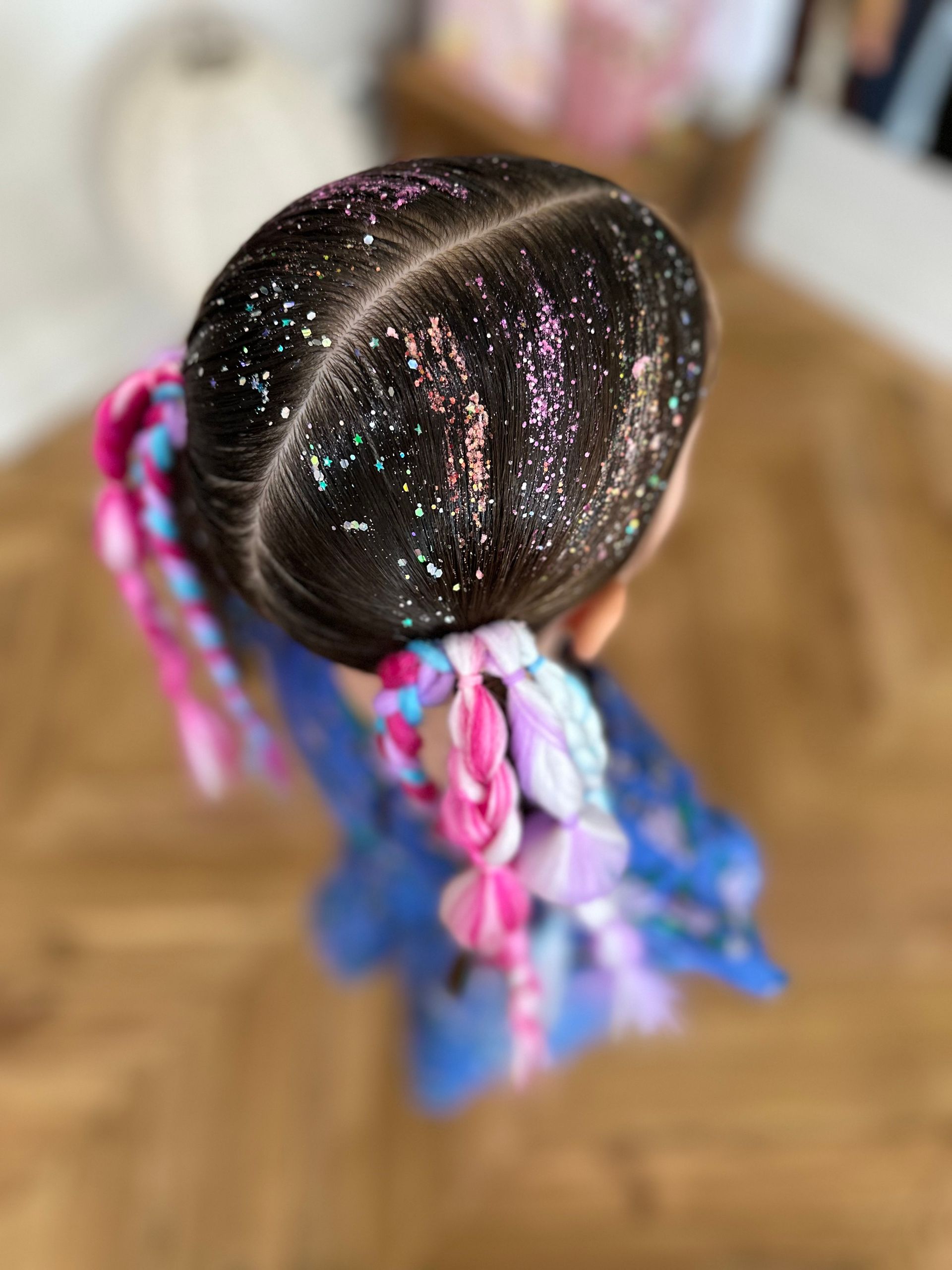 Top view of a childβs dark braided hairstyle with colourful ribbon ties and glitter on hair, indoors β Sweet Parties & Braids in Tatton, NSW