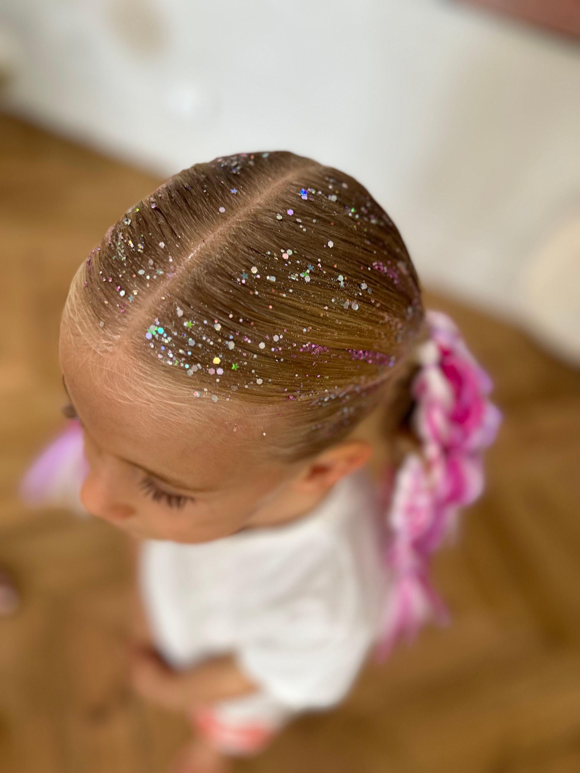 Top view of a child with glittery braided hair and pink accents, wearing a white shirt indoors β Sweet Parties & Braids in Tatton, NSW