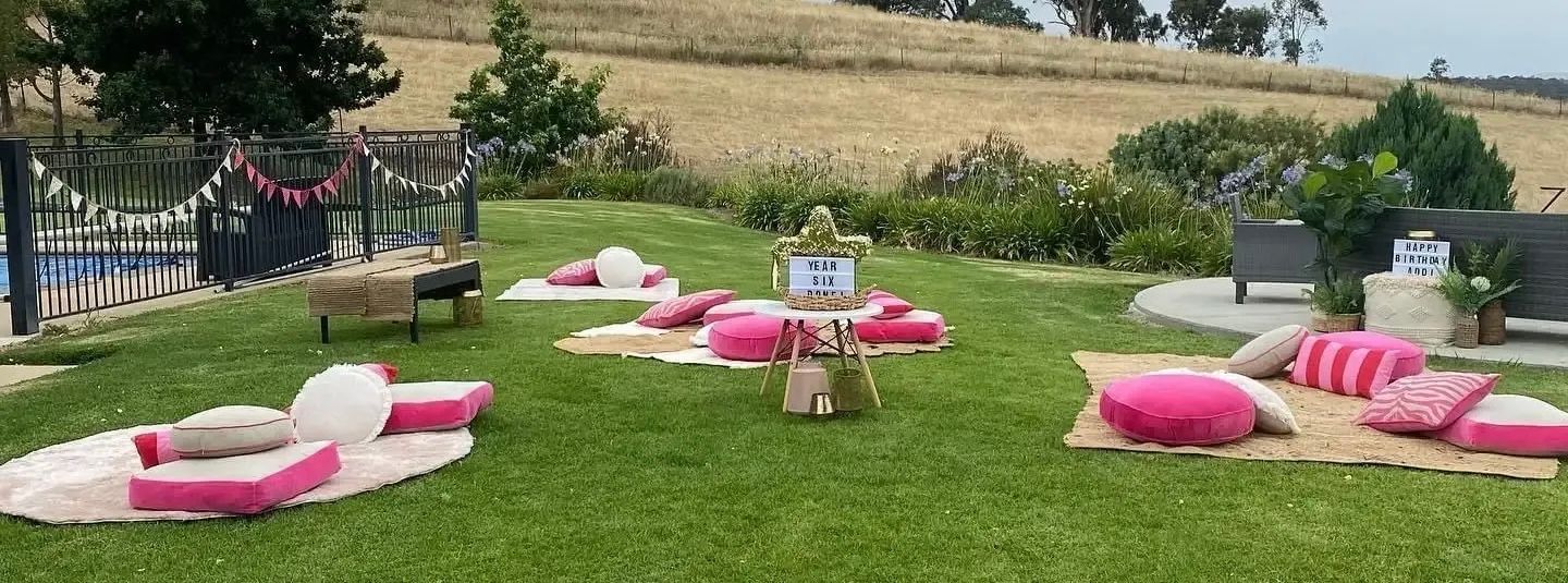 Pink and white picnic cushions arranged on grass in an outdoor garden patio area