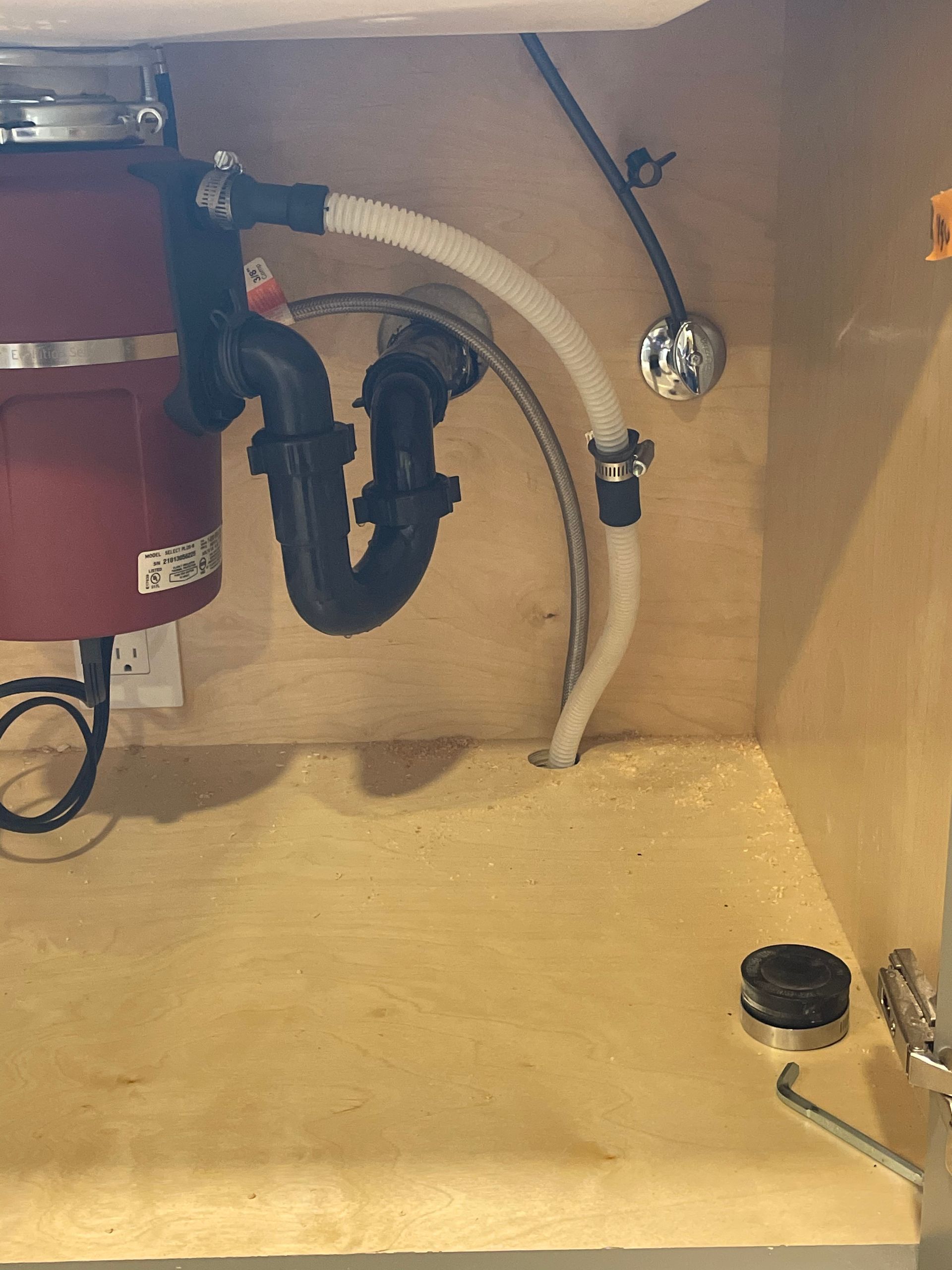 Under-sink plumbing with red appliance, black drain trap, and white hose inside cabinet