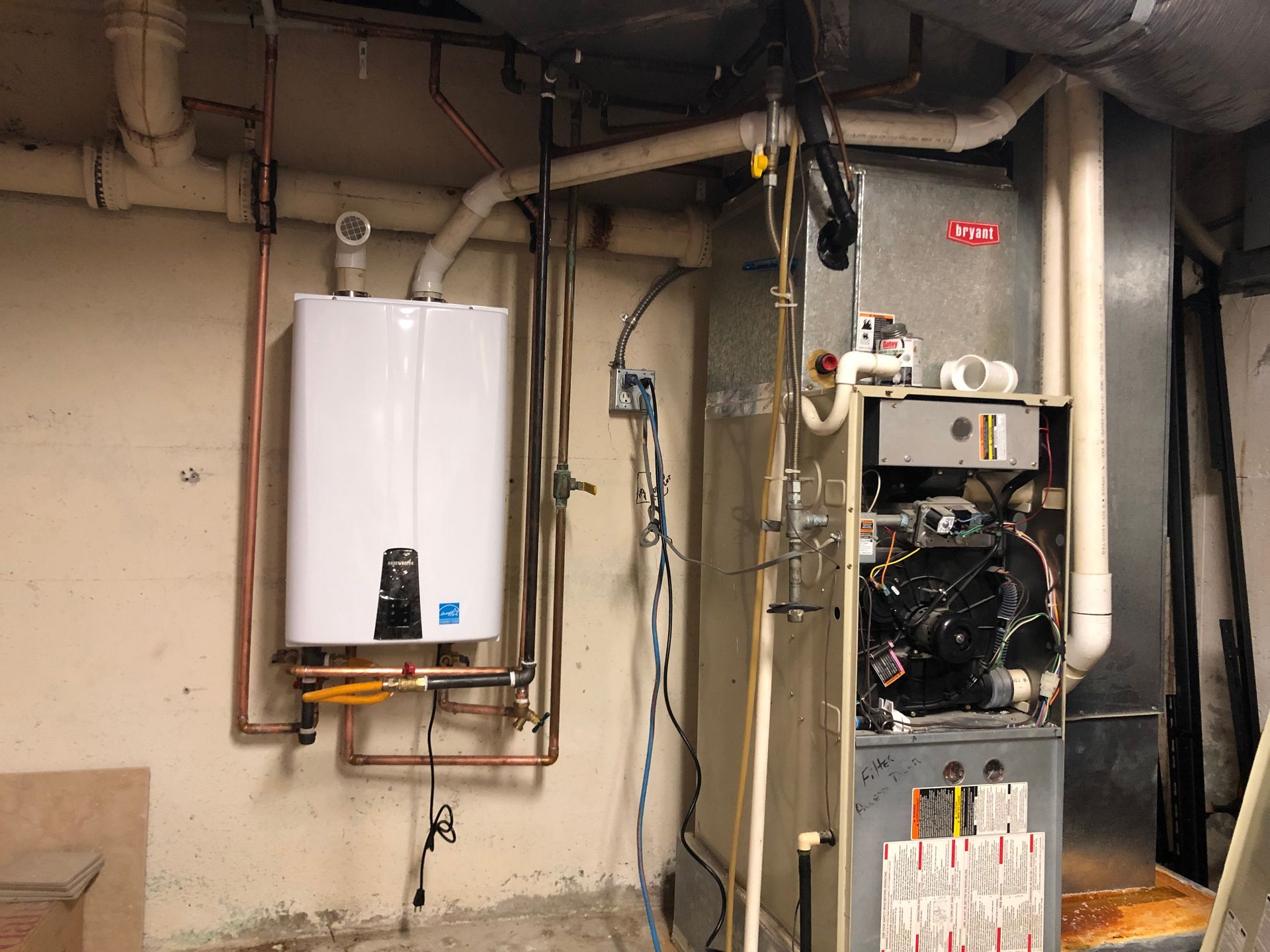 Utility room with wall-mounted water heater, furnace, exposed pipes, and ductwork on a concrete floor.