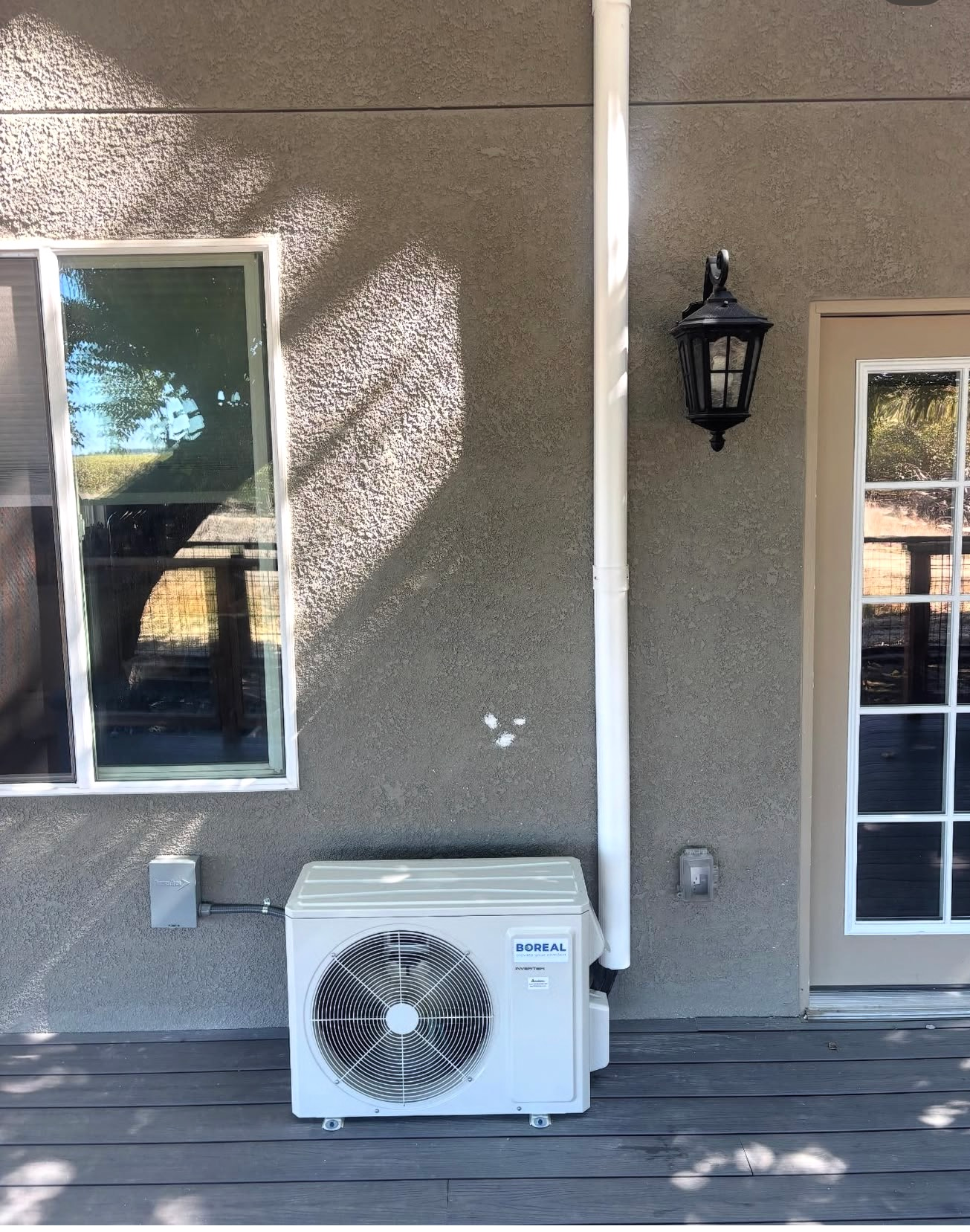 Outdoor patio wall with two windows, a lantern, and a white air-conditioning unit beneath one window