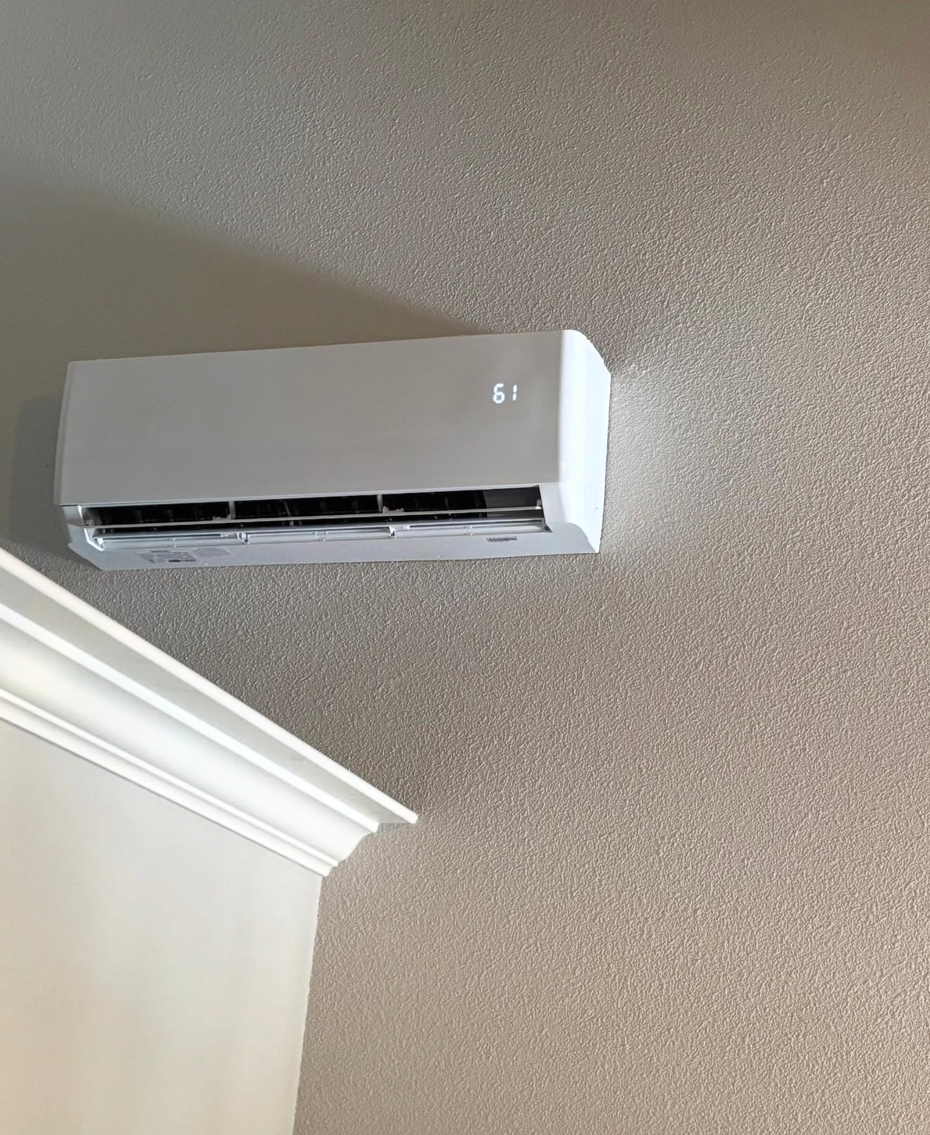 White wall-mounted air conditioner near a ceiling corner on a beige textured wall