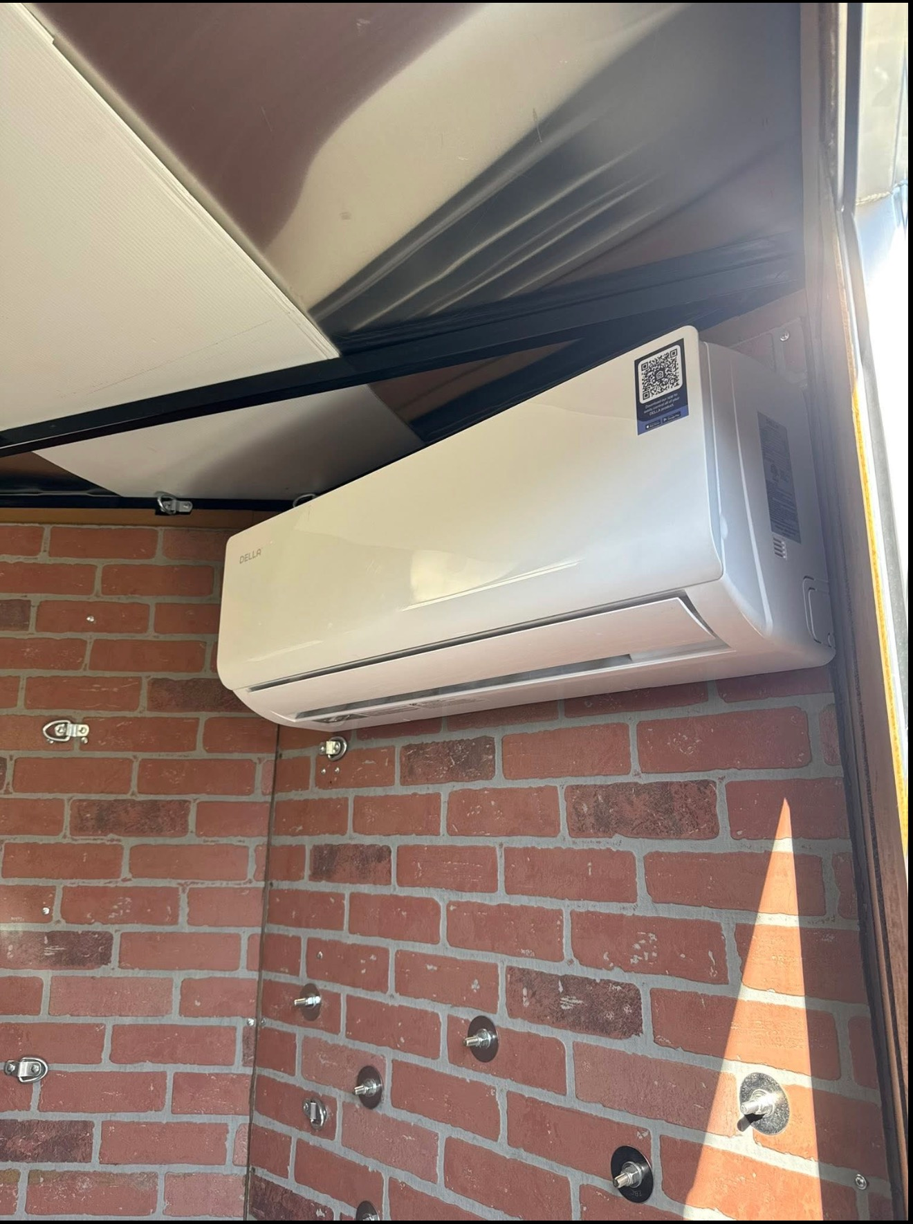 Wall-mounted white air conditioner on a brick exterior wall under a roof overhang.