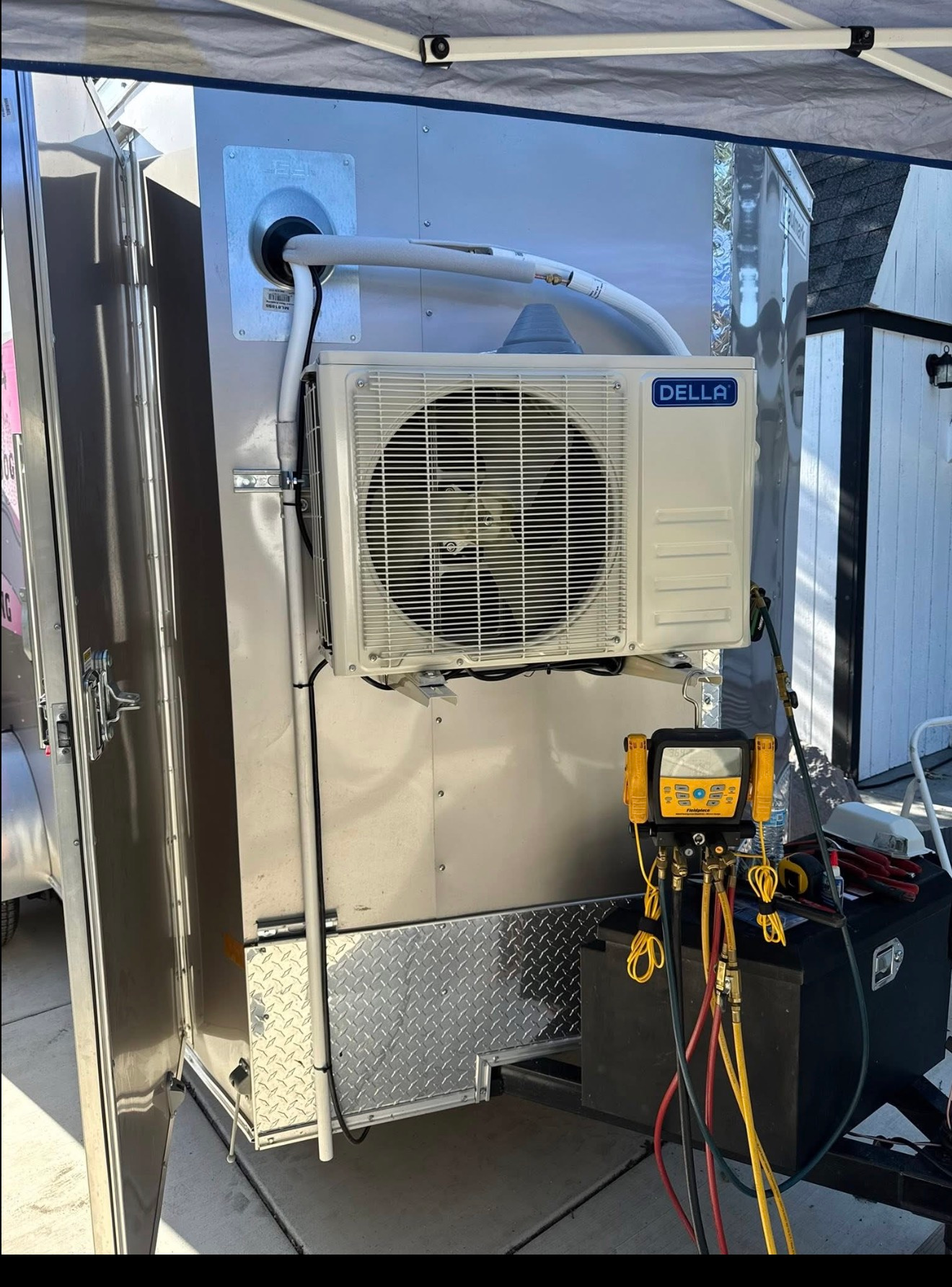 Portable air conditioner under a canopy with a fan grille, hoses, and a control unit beside it