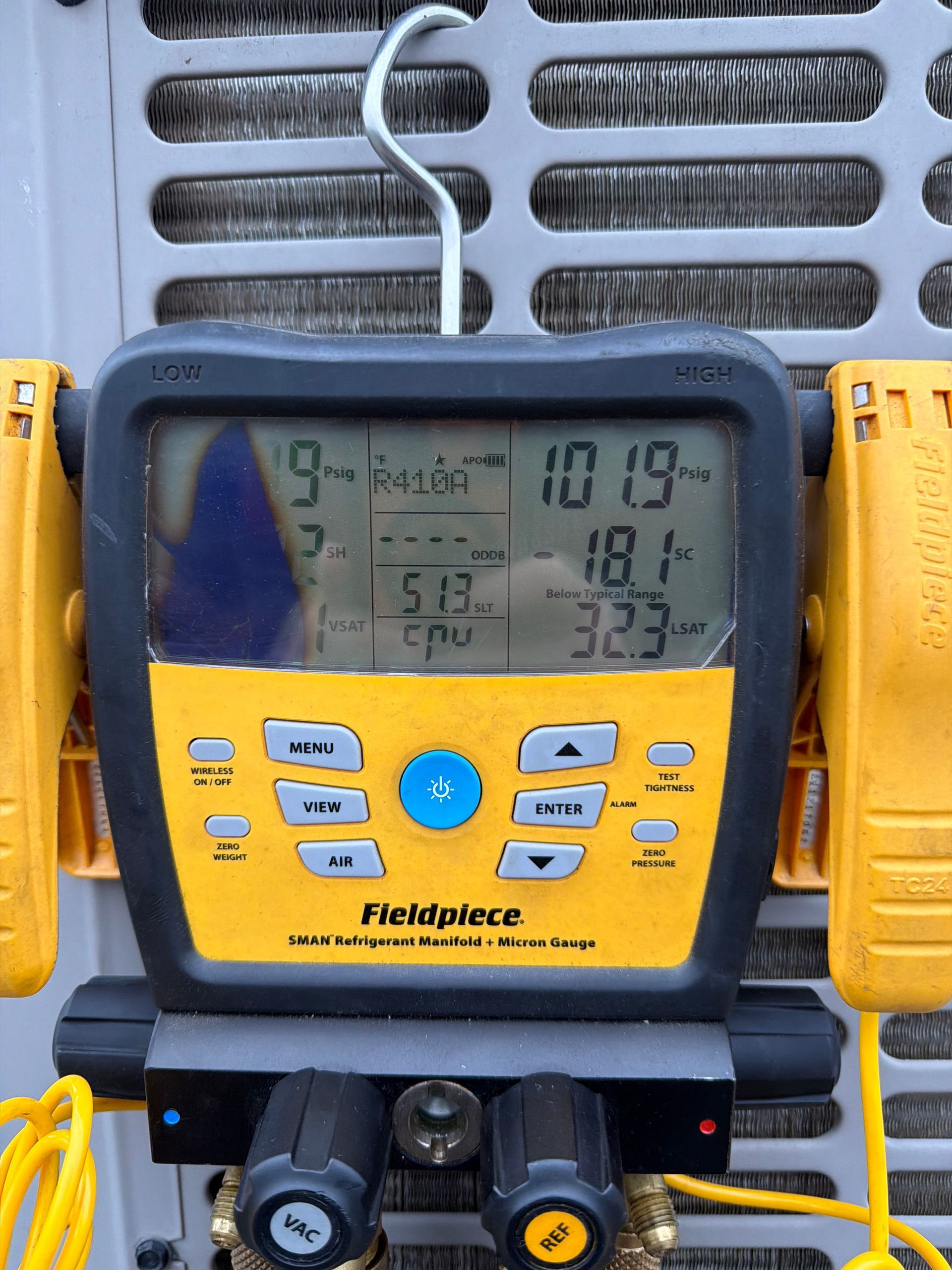 Portable Fieldpiece digital gauge with blue display and yellow casing attached to HVAC equipment.