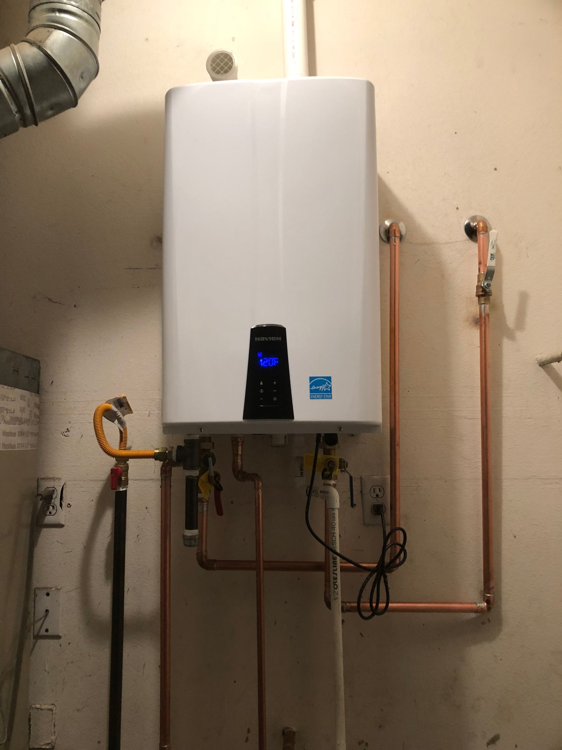 Wall-mounted white boiler with copper pipes and a small digital display in a utility room.