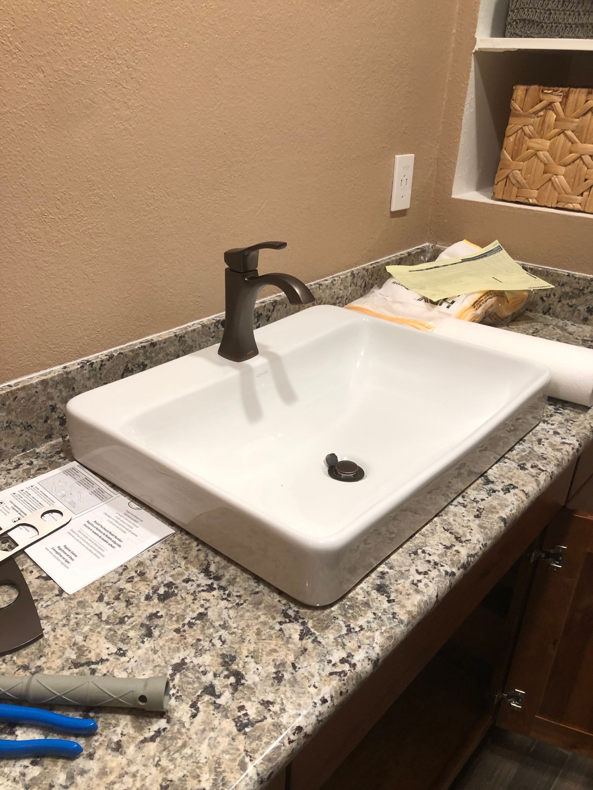 Bathroom sink with black faucet, granite countertop, and a paper towel or plate on the right.