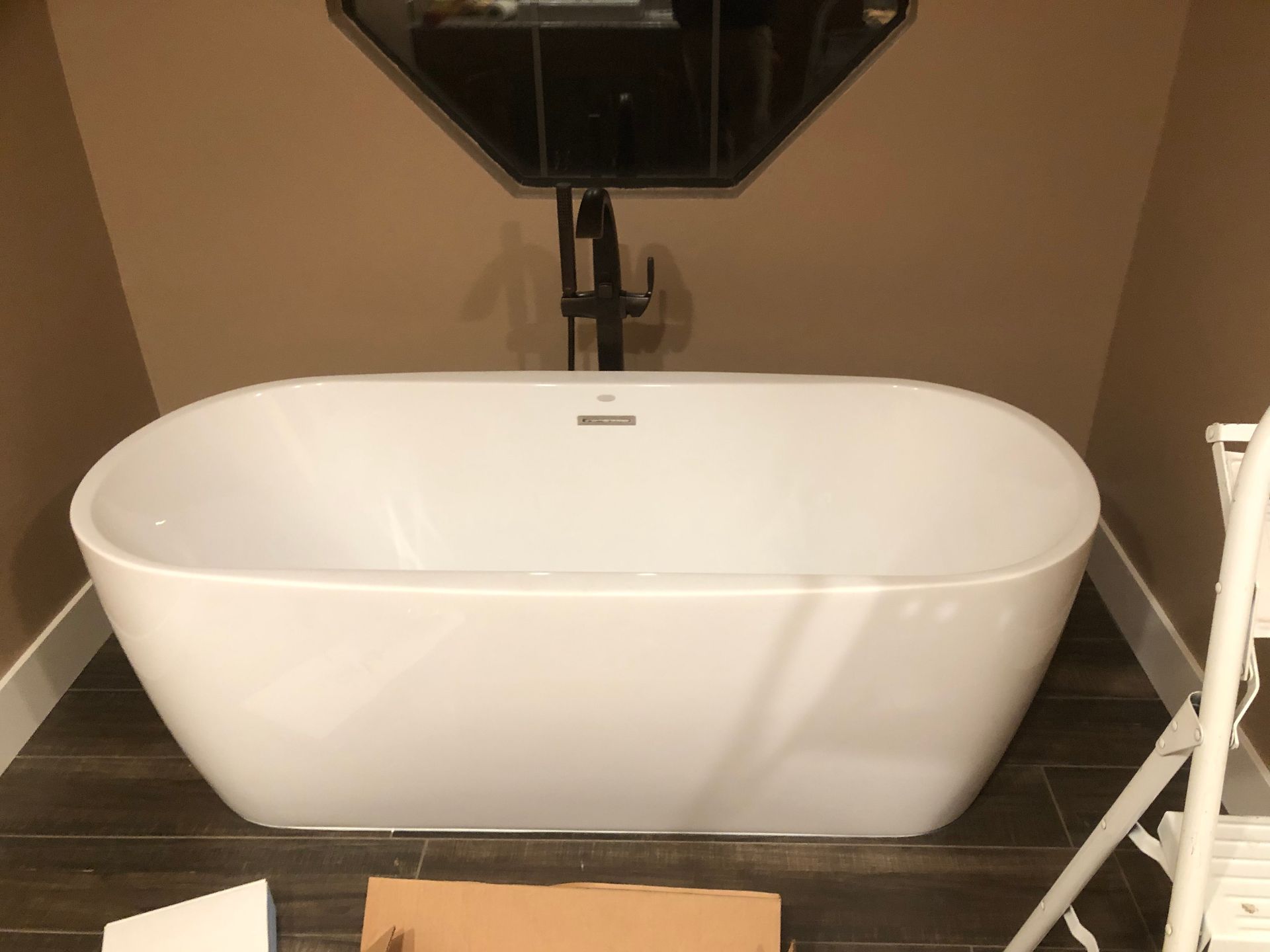 Freestanding white bathtub in a beige bathroom with a wall-mounted faucet and handheld shower.