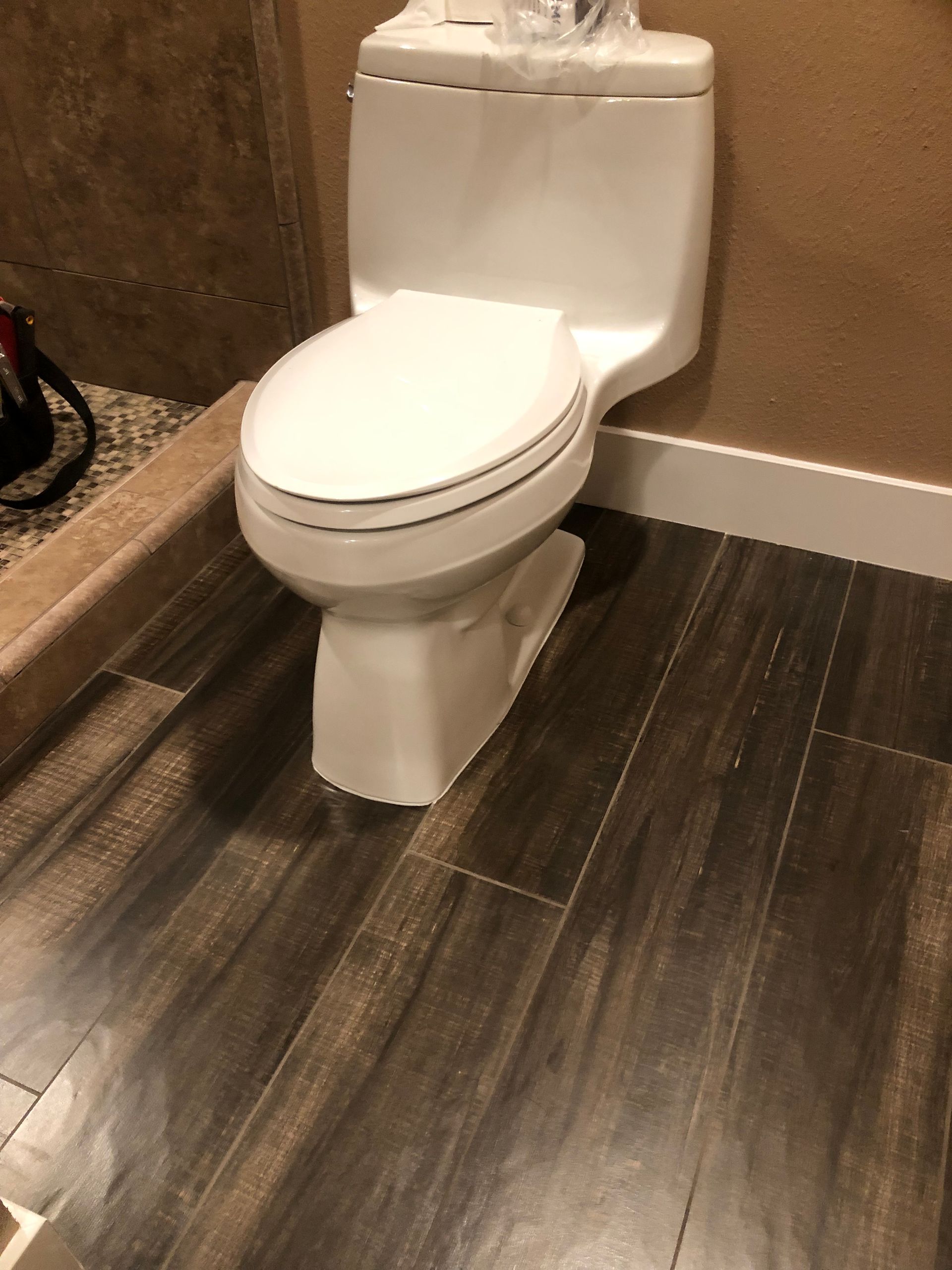 White toilet in a small bathroom with dark wood-look flooring and tan walls
