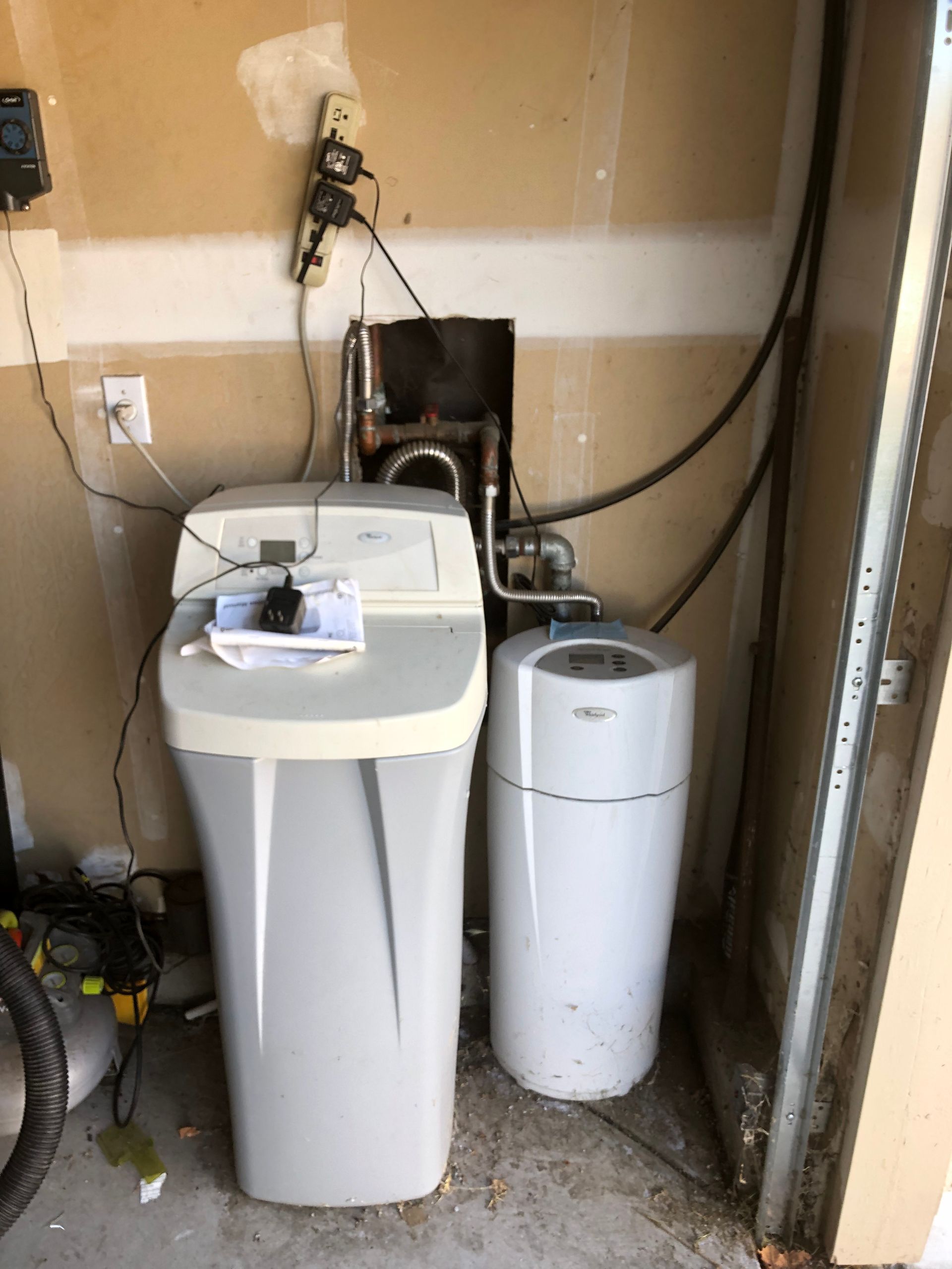Laundry room with a white washer, utility tank, and exposed hoses against unfinished walls