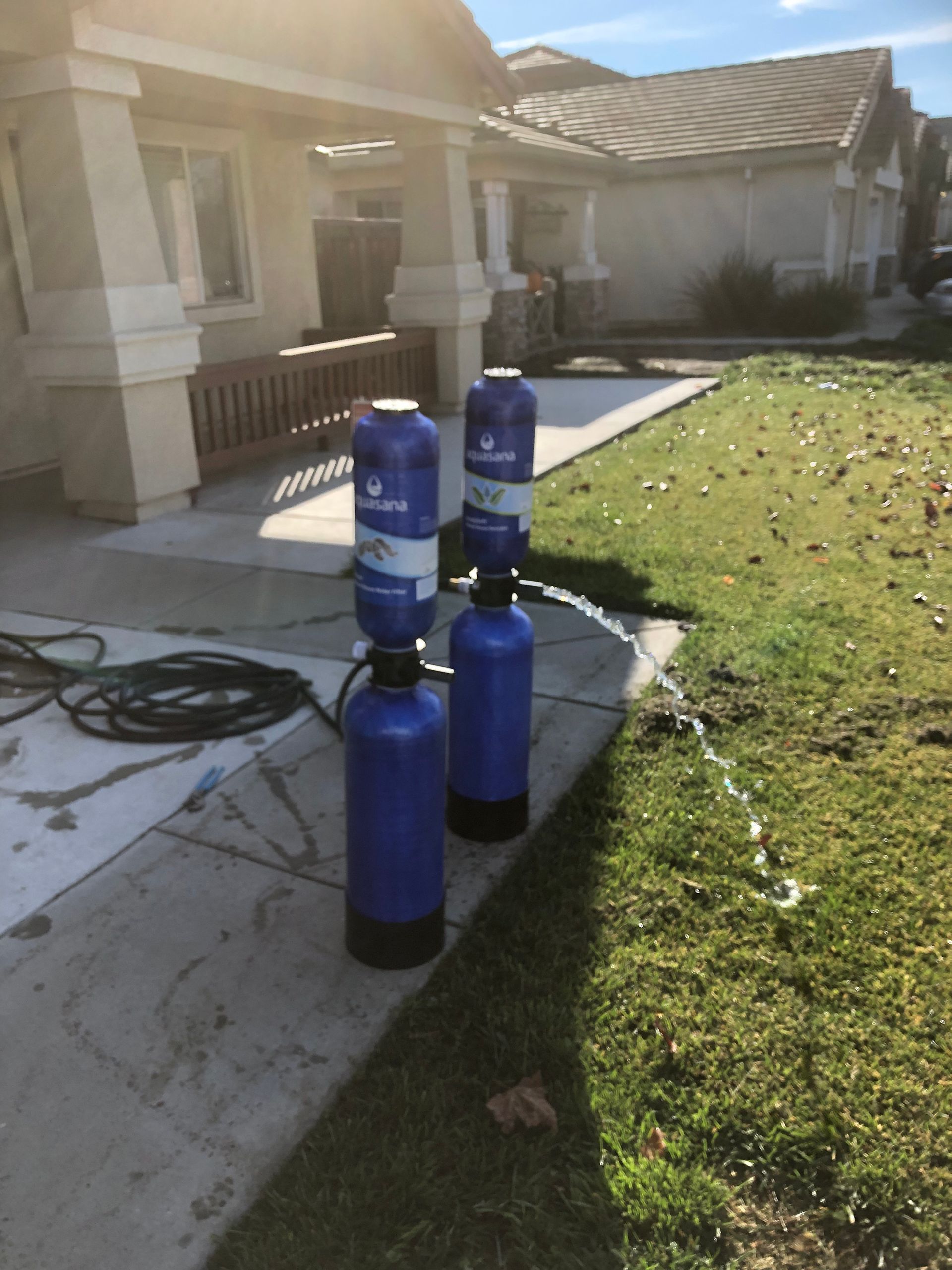 Three blue water filters on a sidewalk beside a house and lawn