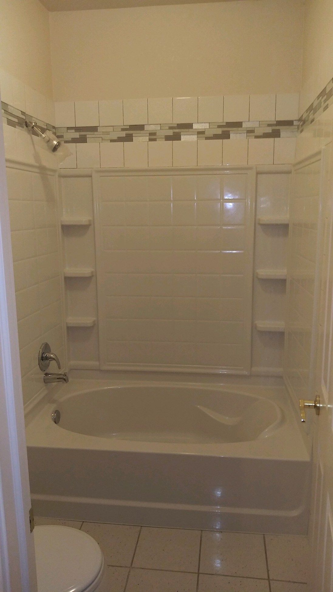 White bathroom with tiled alcove bathtub and built-in corner shelves.
