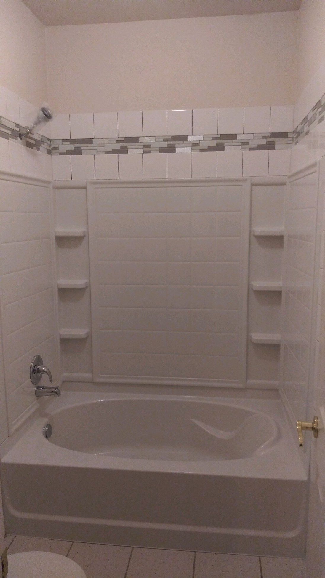 White tiled bathroom with a bathtub, shower surround, built-in shelves, and chrome faucet
