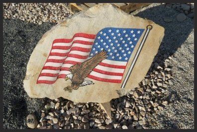 Painted rock with an American flag and eagle on gravel outdoors