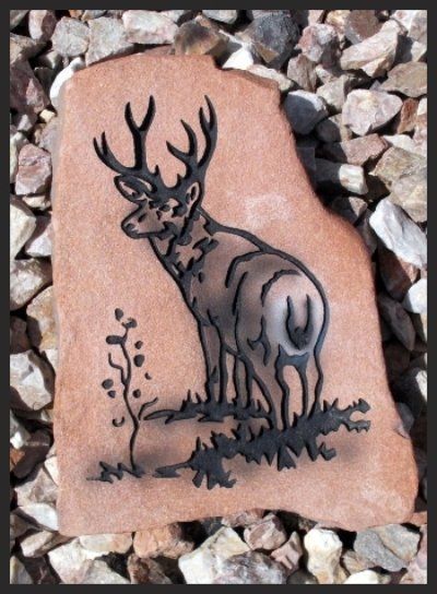 Black deer tattoo sketch on a tan stone among gray gravel.