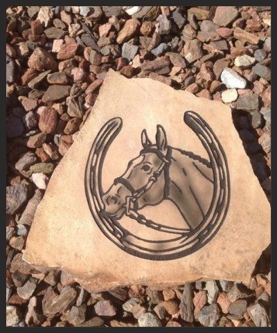 Horse head drawing on a tan rock among reddish gravel, with a horseshoe-like outline.