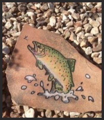 Trout jumping from water, painted on a rock among pebbles.