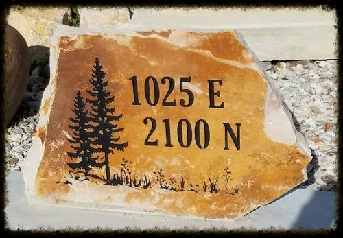 Stone marker with pine tree silhouette and black text reading “1025 E 2100 N” on an orange background.