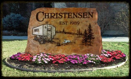 Christensen engraved stone sign with RV, trees, and pink flowers in front of a lawn