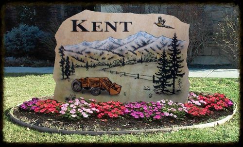Kent entrance sign with mountains, trees, a vintage truck, and pink flowers in front