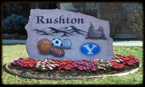 Rushton stone sign with school mascots and flowers in a landscaped memorial garden