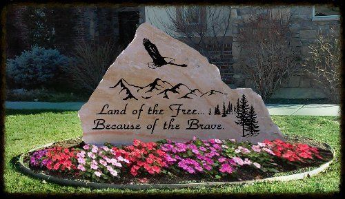 Land of the free, because of the brave engraved on a monument surrounded by pink flowers.