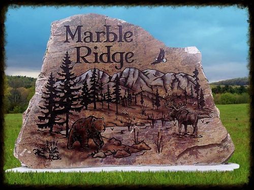 Marble Ridge sign painted on a rock, with trees, deer, and a blue sky background.