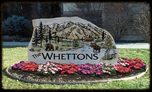 Stone sign reading “THE WHETTONS” surrounded by pink flowers and painted trees