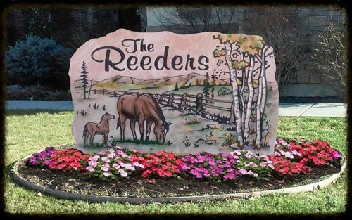 Decorative sign reading “The Feeders” with painted deer, set in a flower bed outdoors