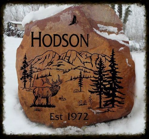 Hodson sign on a carved rock with mountains, trees, a moose, and “Est 1972” text