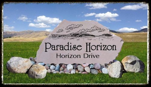 Paradise Horizon sign on a stone monument in a grassy field with mountains and blue sky behind