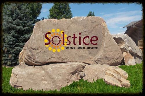 Solstice community sign on a large boulder in front of grass and trees