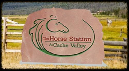 The Horse Station at Cache Valley sign on a pink rock-shaped plaque in a fenced pasture