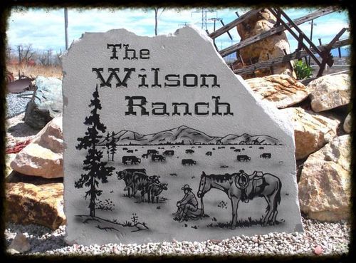 The Wilson Ranch engraved on a stone sign with desert landscape and horses