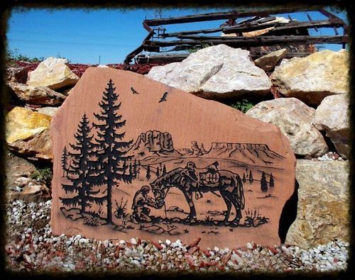 Engraved rock art of a horse and rider on a red stone amid stacked boulders under blue sky