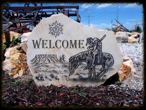 Stone welcome sign with cowboy on horseback in a rustic outdoor setting under blue sky