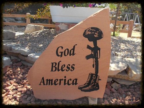 Stone sign reading “God Bless America” beside a soldier silhouette in an outdoor garden setting