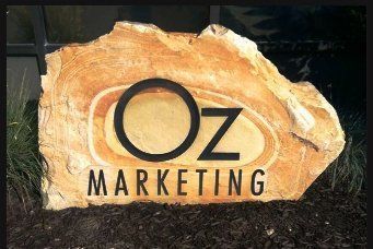 Oz Marketing logo on a tan stone sign outdoors