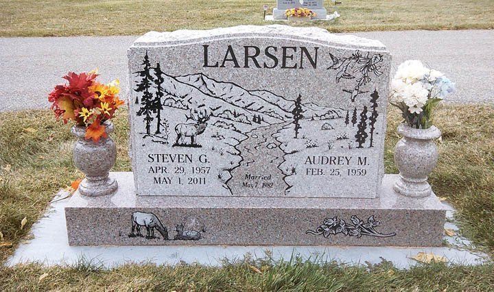 Gravestone with “LARSEN” engraved, flanked by flower vases, in a cemetery setting.