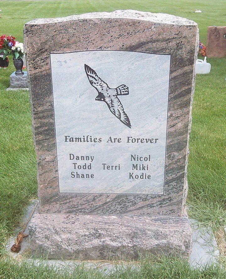 Stone memorial headstone with engraved bird and names in a grassy cemetery.