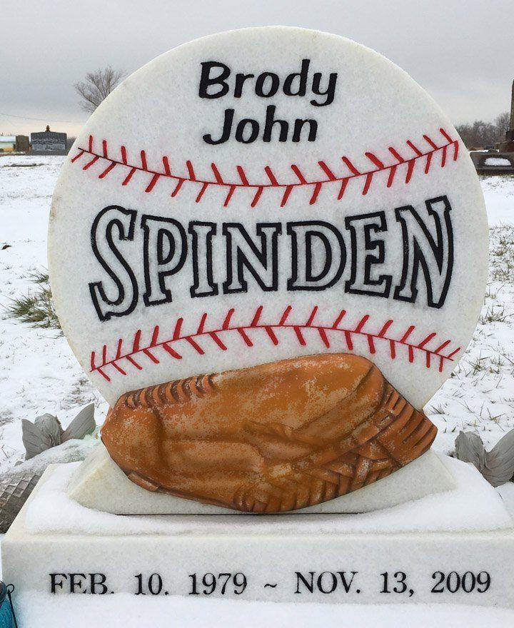 Snow-covered baseball-shaped grave marker for Brody John Spinden with dates and glove sculpture.