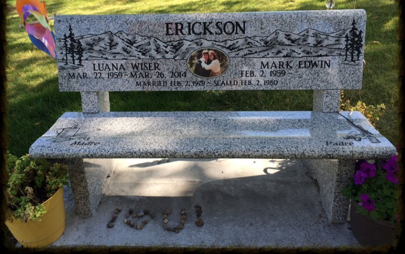 Stone memorial bench with flowers and engraved names in a grassy cemetery