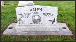 A gray gravestone in a grassy cemetery, engraved with the name Allen and floral and cross designs.