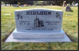 Gray granite cemetery headstone with the name “Nielsen” engraved in front of a grassy lawn.