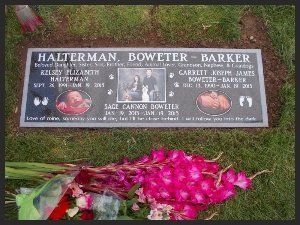 Gravestone plaque on grass with engraved names and pink flowers laid below it
