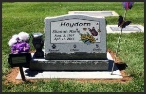 Gravestone with flowers and a purple memorial arrangement in a grassy cemetery plot