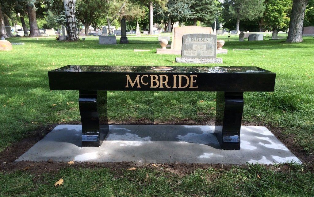Black memorial bench engraved “MCBRIDE” in a grassy cemetery or park setting